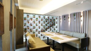 A modern meeting room with a long table, two sofas, and a wall of potted plants. - Ramedo Hotel (Makassar)