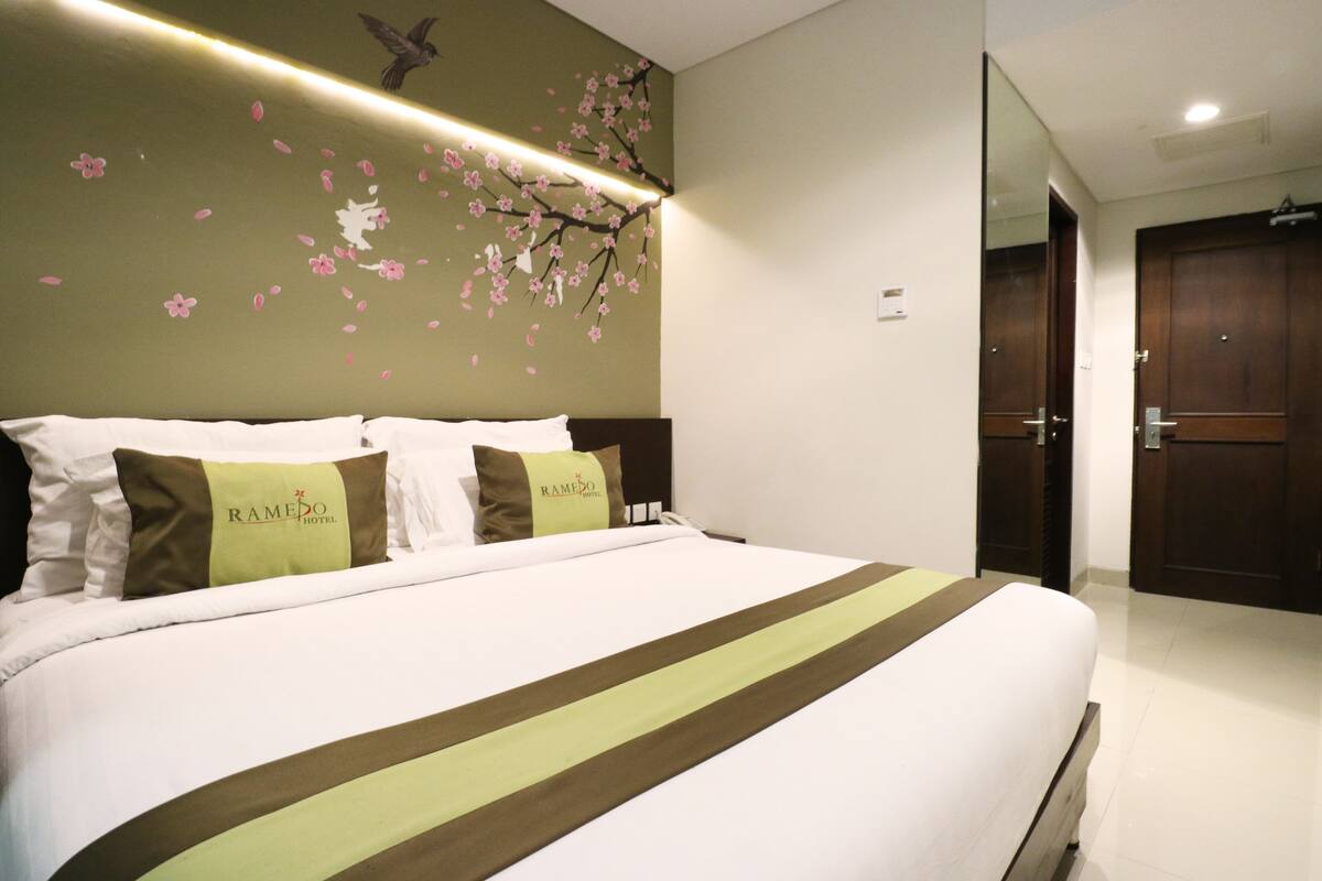 A hotel room with a bed, pillows, a wall with a floral design, and a door.