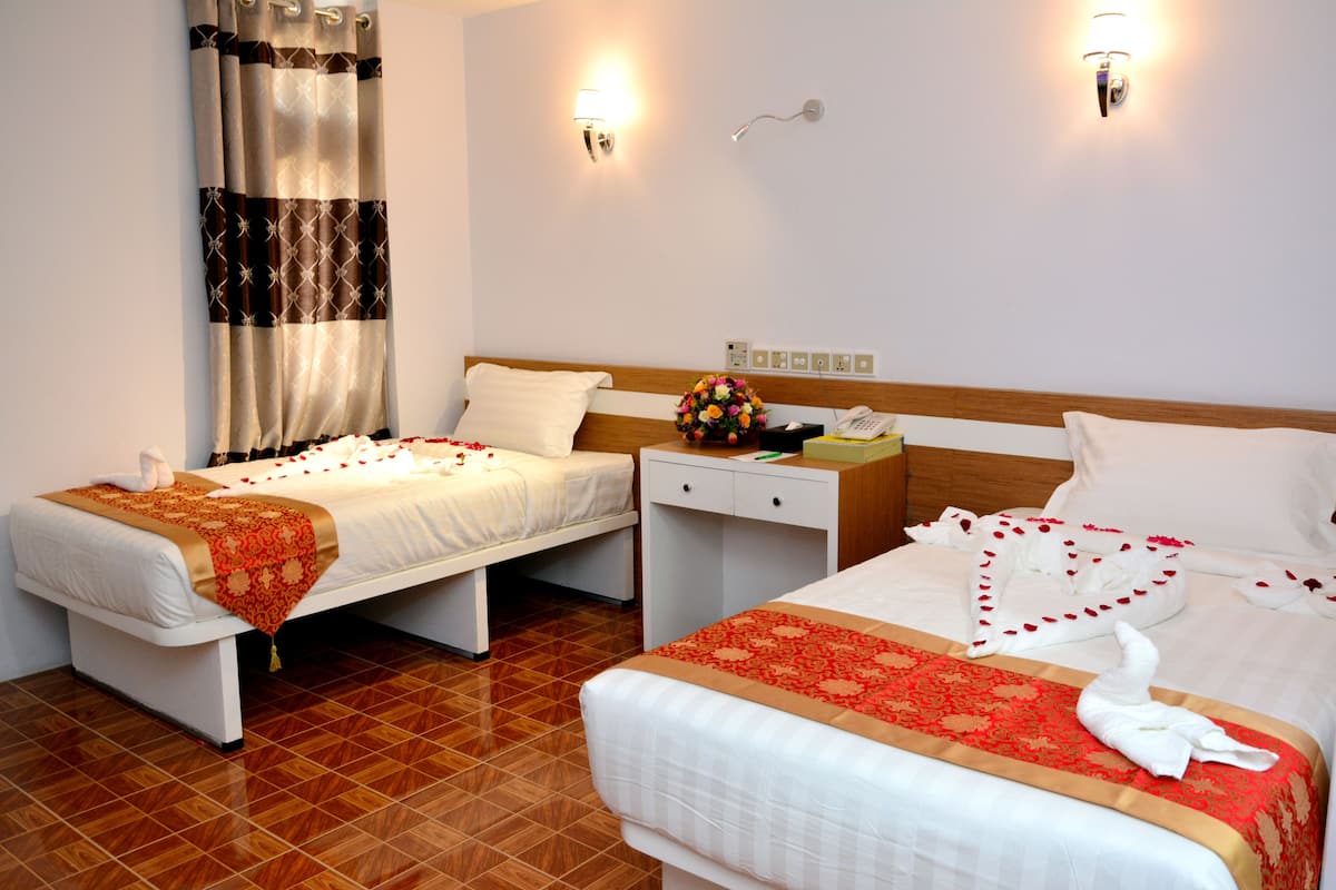 A hotel room with two beds, a nightstand, a lamp, and a flower arrangement.