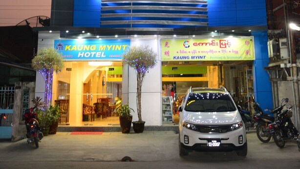 Exterior del hotel Kaung Myint, con diseño moderno, señalización iluminada y un coche estacionado frente al hotel.