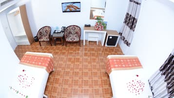 Une chambre d’hôtel avec deux lits, un bureau, des chaises, une télévision et une petite table sur laquelle est posé un vase avec des fleurs.