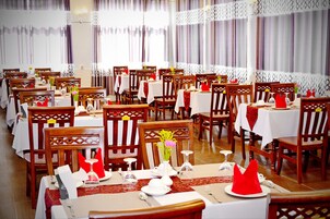 Un restaurante con varias mesas y sillas, cada juego con manteles blancos, servilletas rojas y un jarrón con flores.