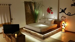 Une chambre à coucher moderne, avec un lit, une télévision, une plante décorative et un luminaire fixé au mur.