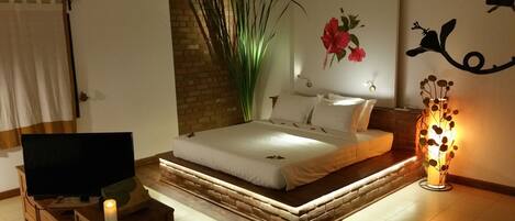 A modern bedroom with a bed, a TV, a decorative plant, and a wall-mounted light fixture.