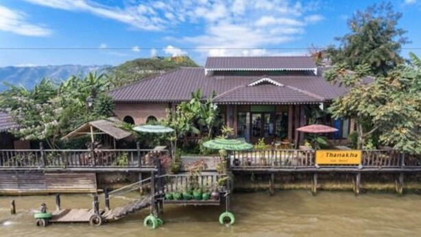 Un bâtiment traditionnel avec un toit en tuiles, entouré de verdure et bordé d’un plan d’eau.