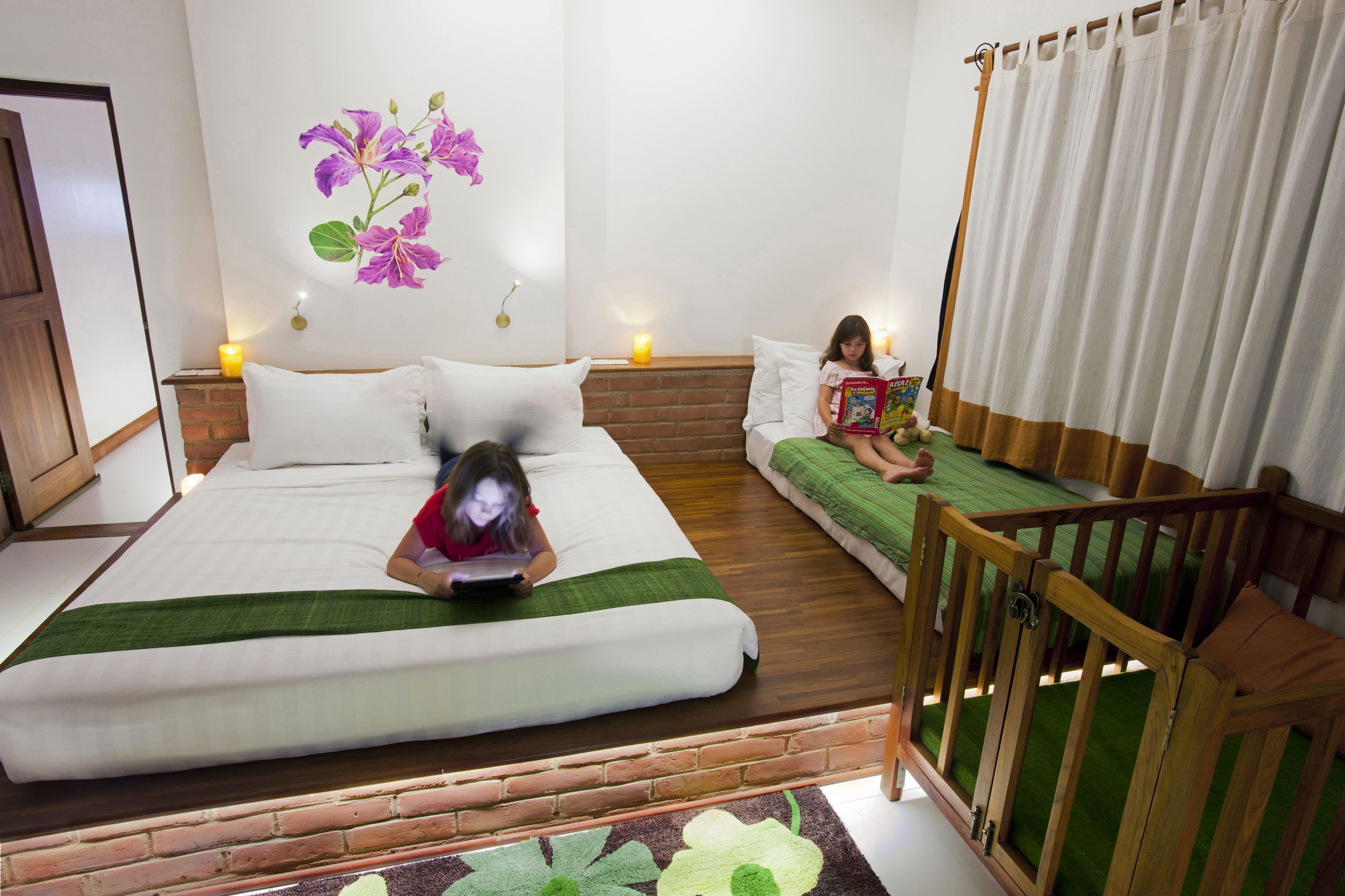 Una habitación con una cama grande, una cama más pequeña, una cuna de madera y una pared con un mural floral.