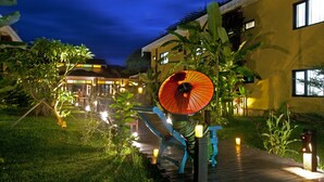 Un espace extérieur bien éclairé, avec un chemin, un parasol décoratif et un bâtiment doté de nombreuses fenêtres.