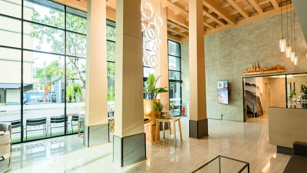 A modern lobby with large windows, a reception desk, and a seating area with tables and chairs.