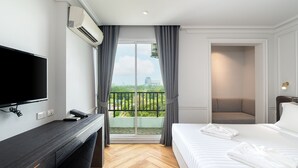 A hotel room with a bed, a TV, a desk, and a balcony with a view of the city.