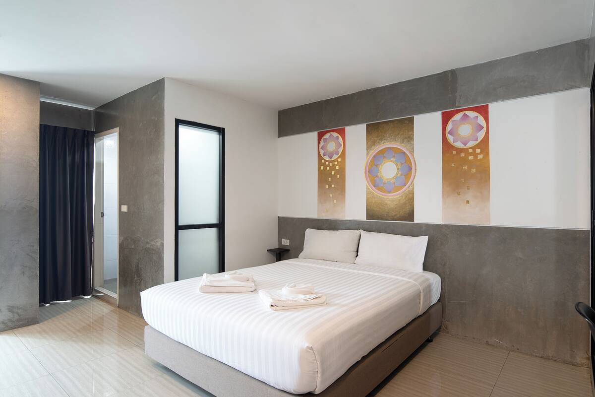 A modern hotel room with a large bed, a nightstand, and a view of the hallway.