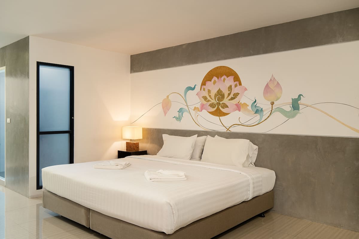 A neatly made bed with white linens, a wall-mounted lamp, and a large floral artwork above the bed.