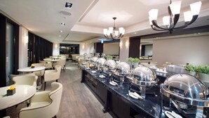A buffet setup with multiple round tables and chairs, a long counter with food service equipment, and a chandelier. - 53 Hotel (Taichung)