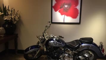 A motorcycle parked indoors with a framed artwork of a red flower on the wall behind it.