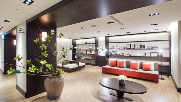 A modern hotel lobby with a wooden floor, a central seating area with a sofa and armchairs, a coffee table, and a large vase with green plants. - 53 Hotel (Taichung)