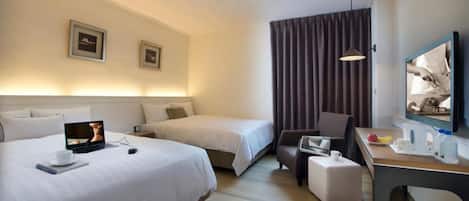 A hotel room with two beds, a desk with a laptop, a chair, a TV, and a curtain.