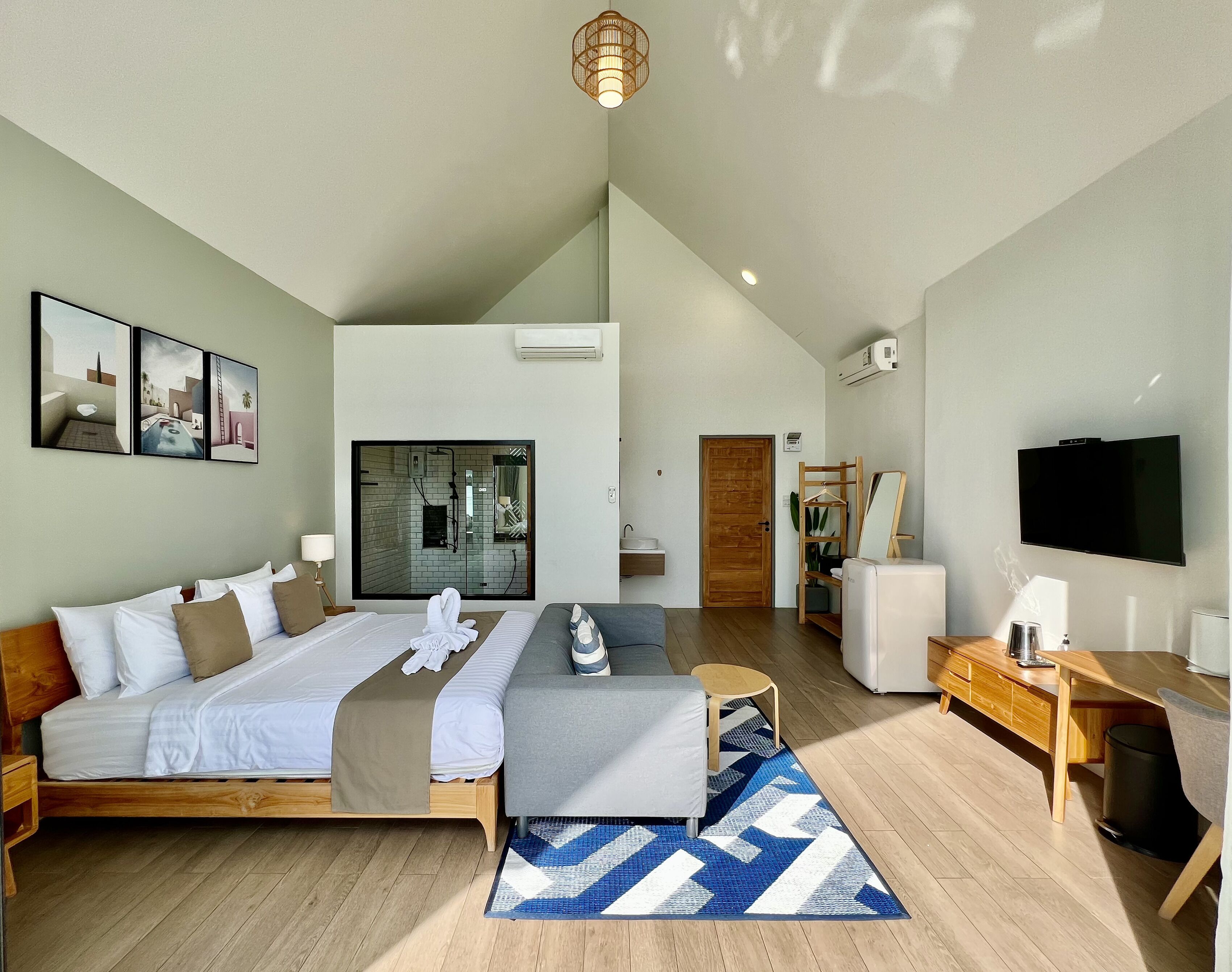 A modern hotel room with a large bed, a desk, a TV, and a bathroom with a glass shower enclosure.