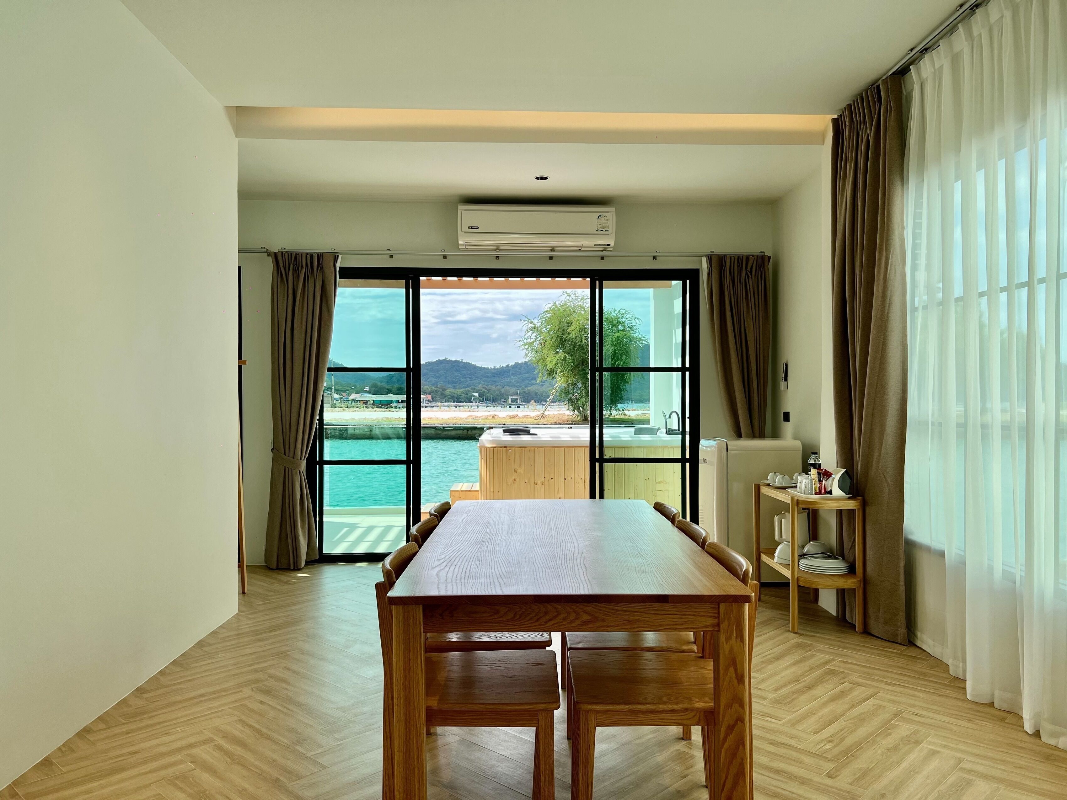 Une pièce spacieuse avec une table à manger en bois, une vue sur un plan d’eau et un balcon doté d’un jacuzzi.