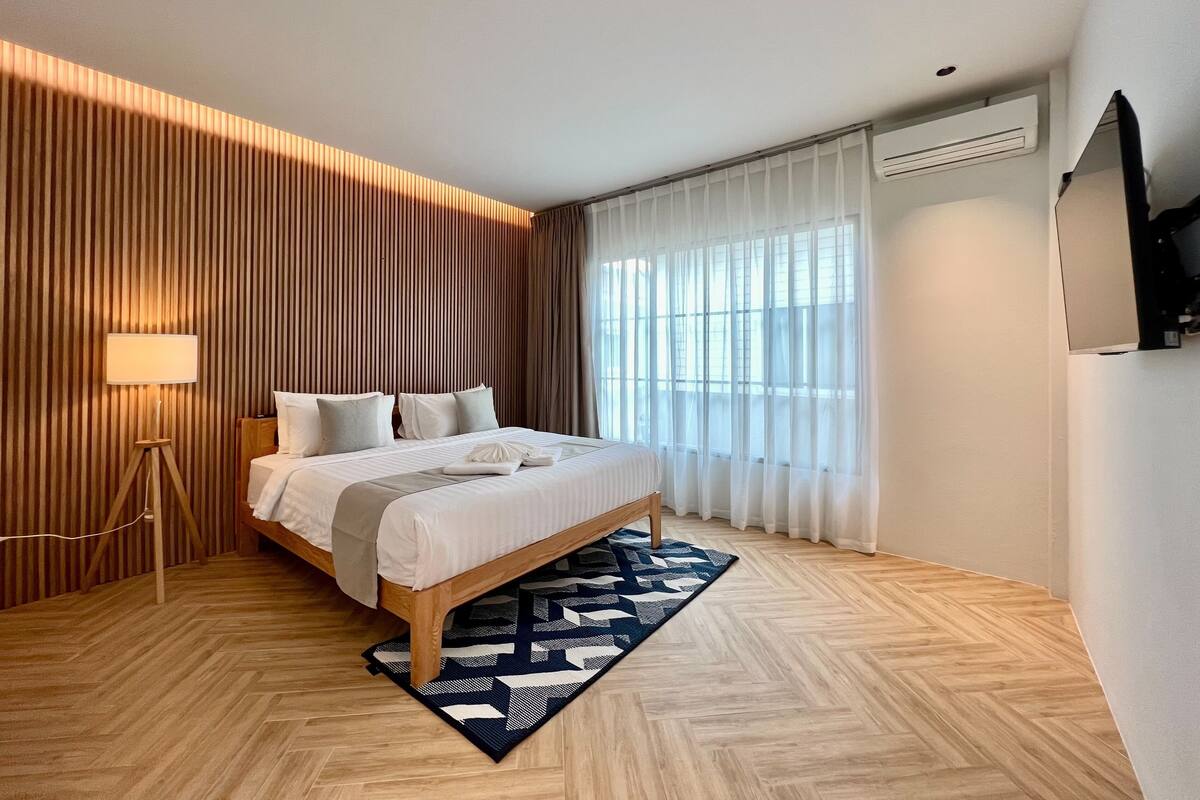 Een moderne hotelkamer met een groot bed, een staande lamp en een visgraatvloer.