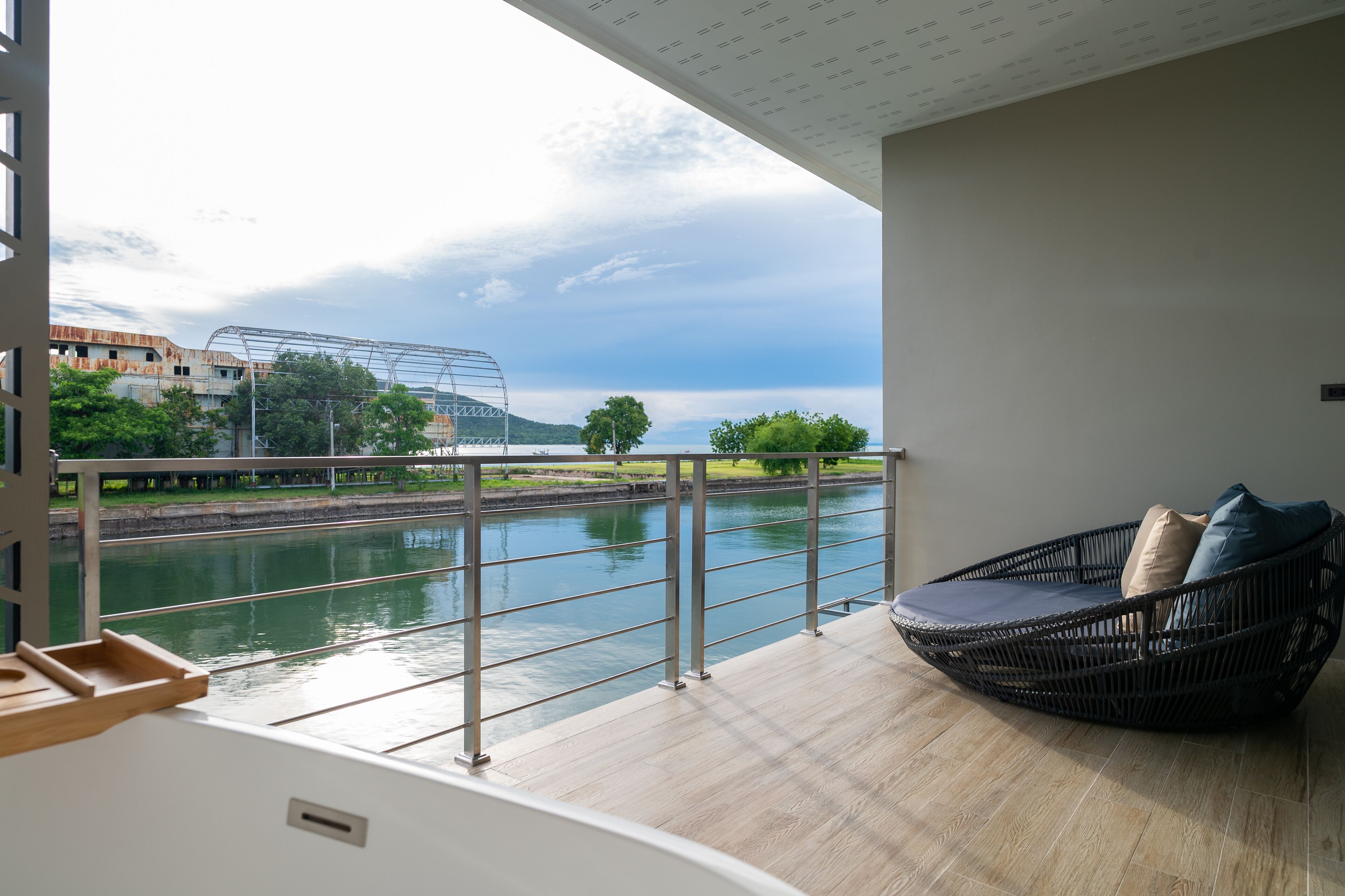 A balcony with a view of a river, a metal railing, and a wicker chair with cushions.