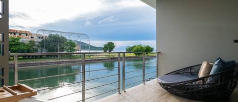 A balcony with a view of a river, a metal railing, and a wicker chair with cushions.