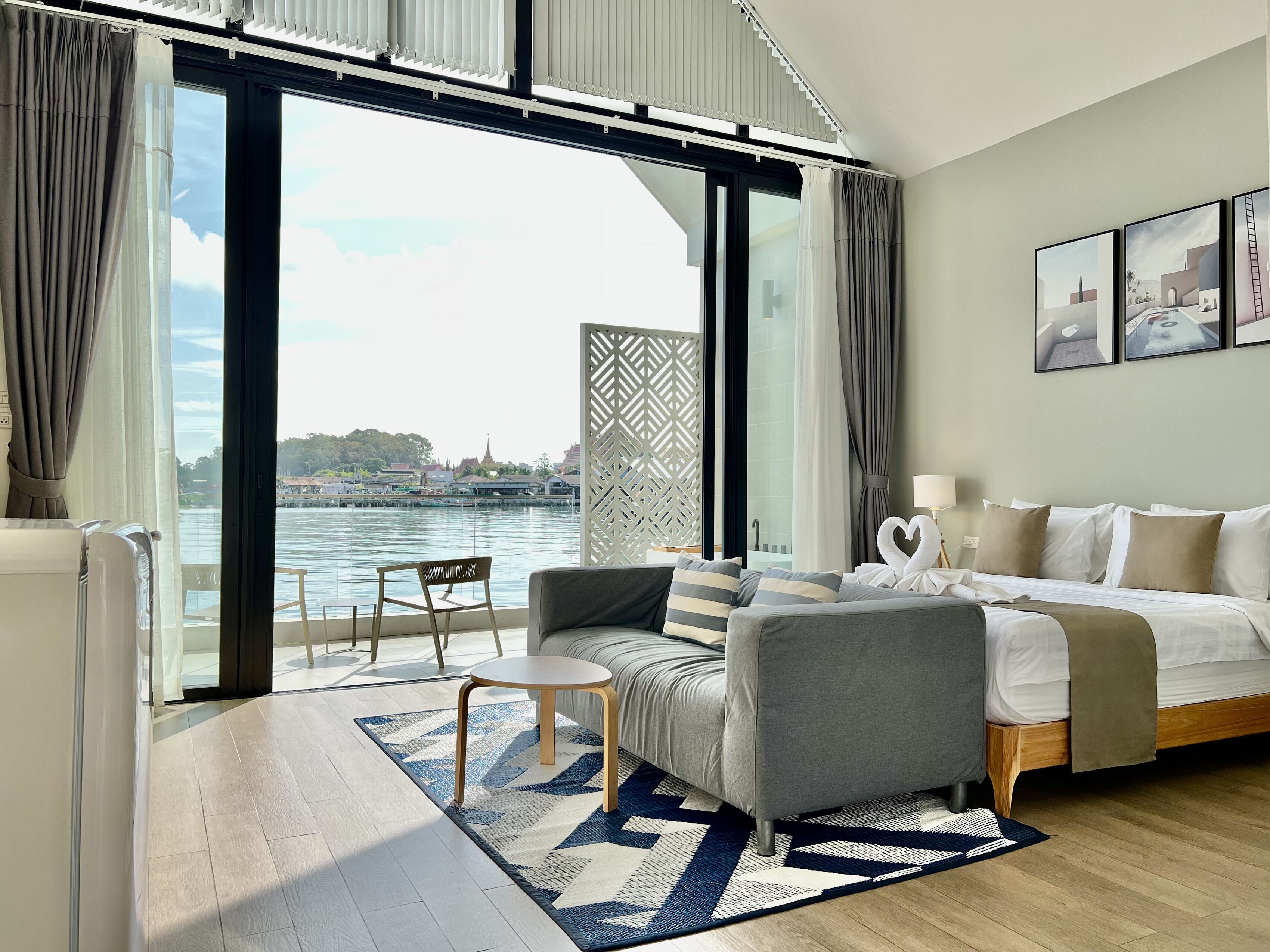 Een moderne hotelkamer met een grote schuifglazen deur naar uitzicht op het water, een bank, een kleine tafel en een bed in een wit-beige kleurenschema.