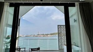 Un balcón con dos sillas, vista al mar y un edificio a lo lejos.