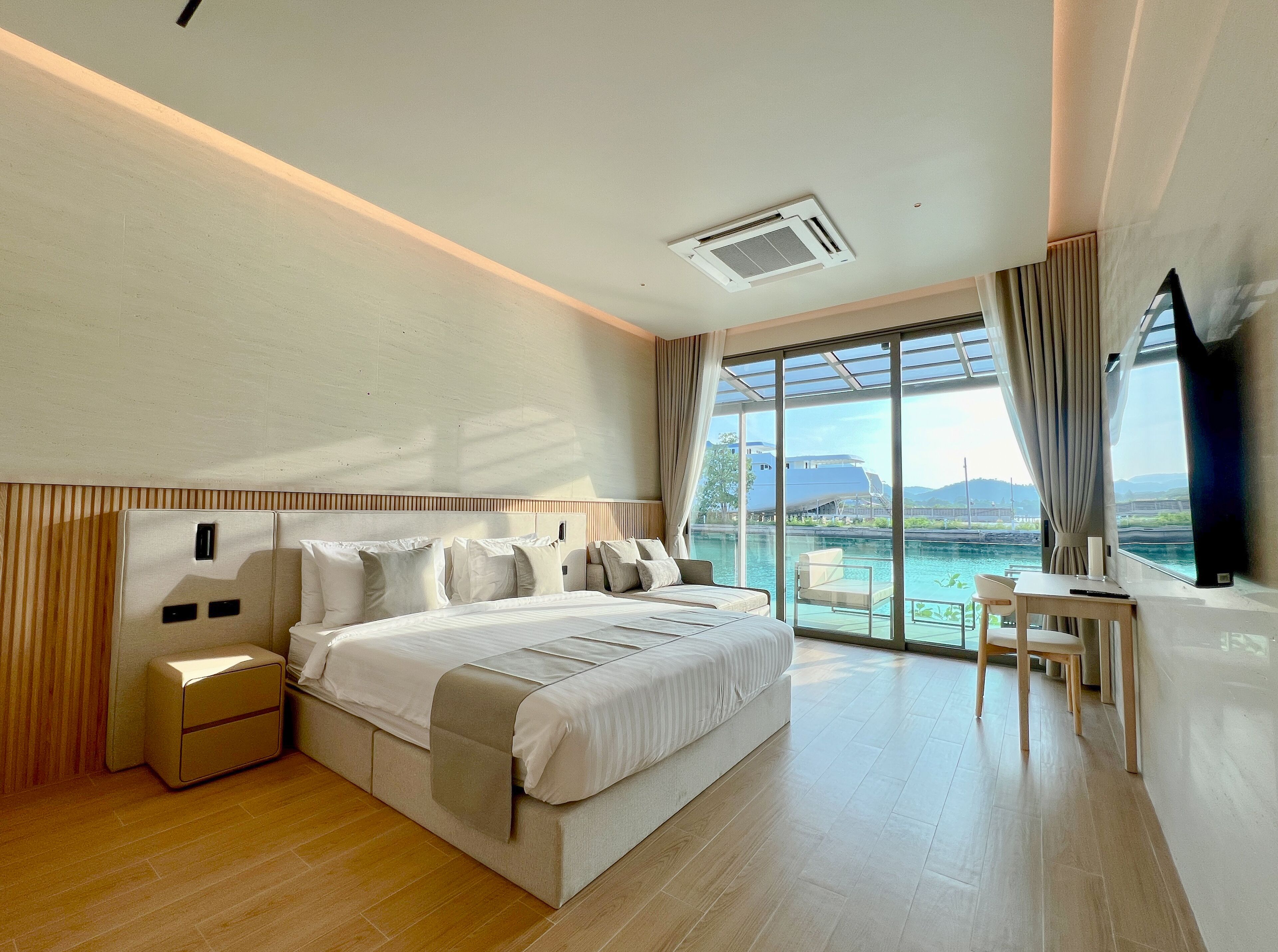 A modern hotel room with a large bed, a desk, and a view of a body of water.