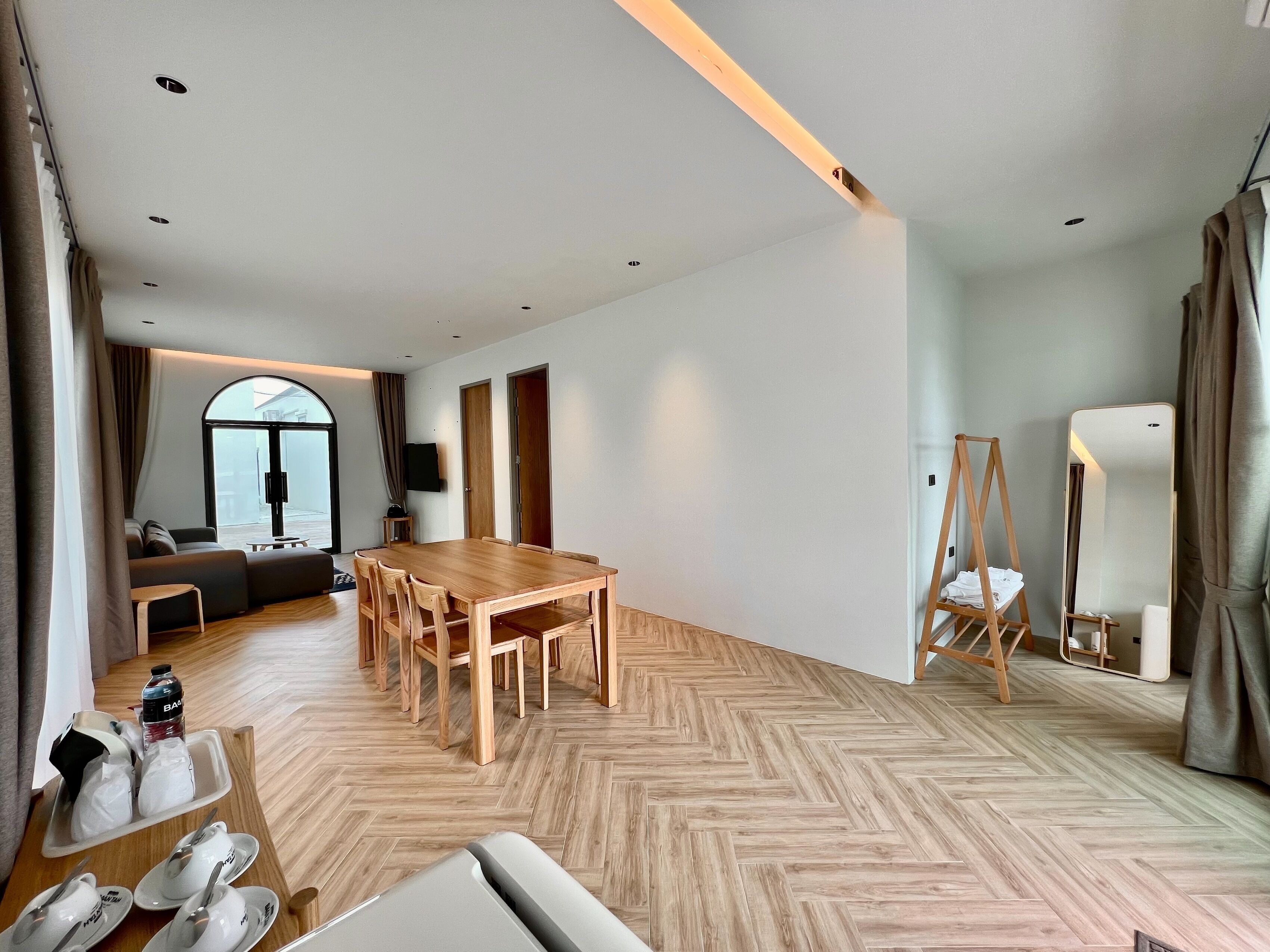 A modern living room with a wooden dining table, sofa, and a large mirror.