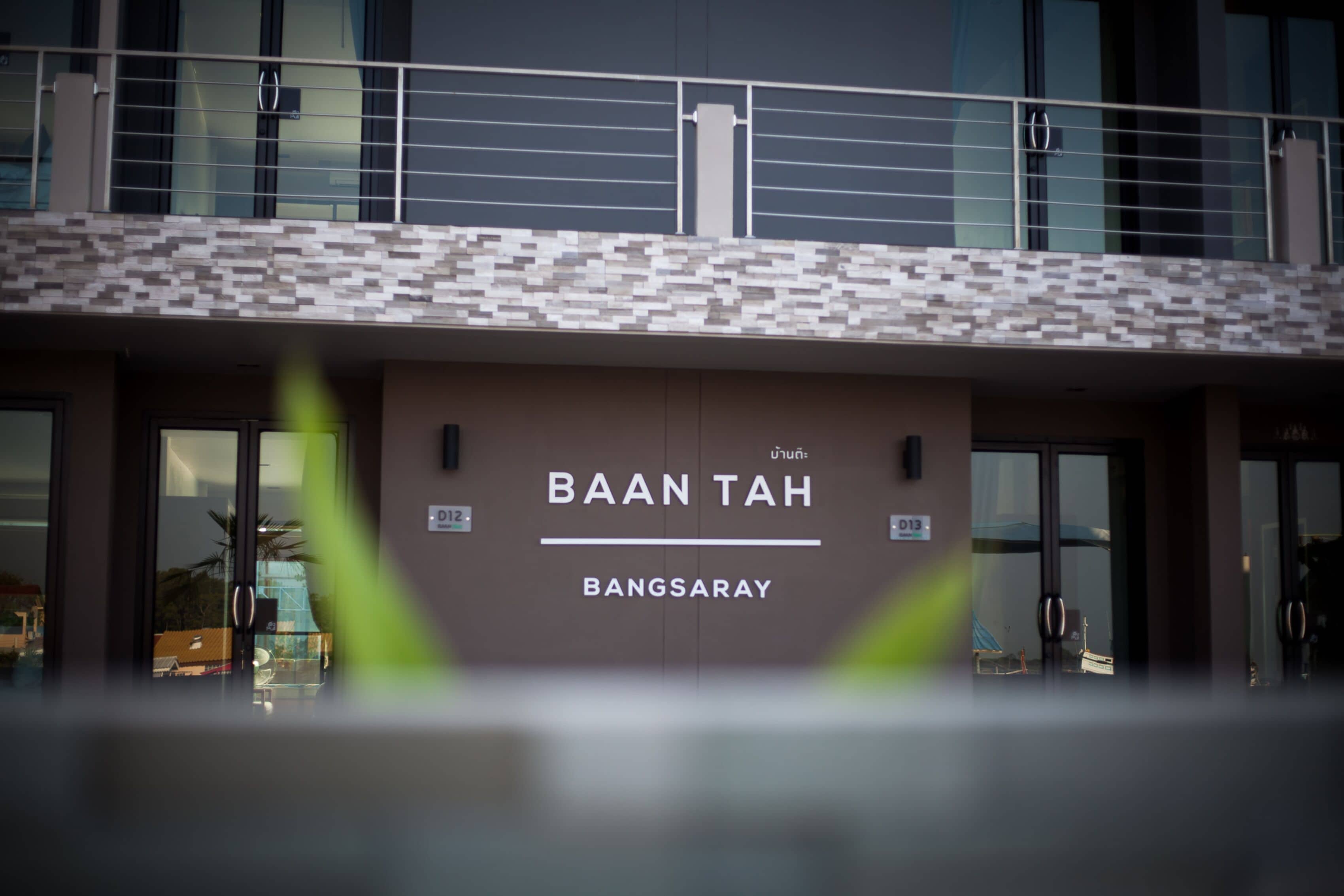 Un edificio con un cartel que dice "BAAN TAH BANGSARAY" y un diseño arquitectónico moderno con fachada estampada y ventanas grandes.