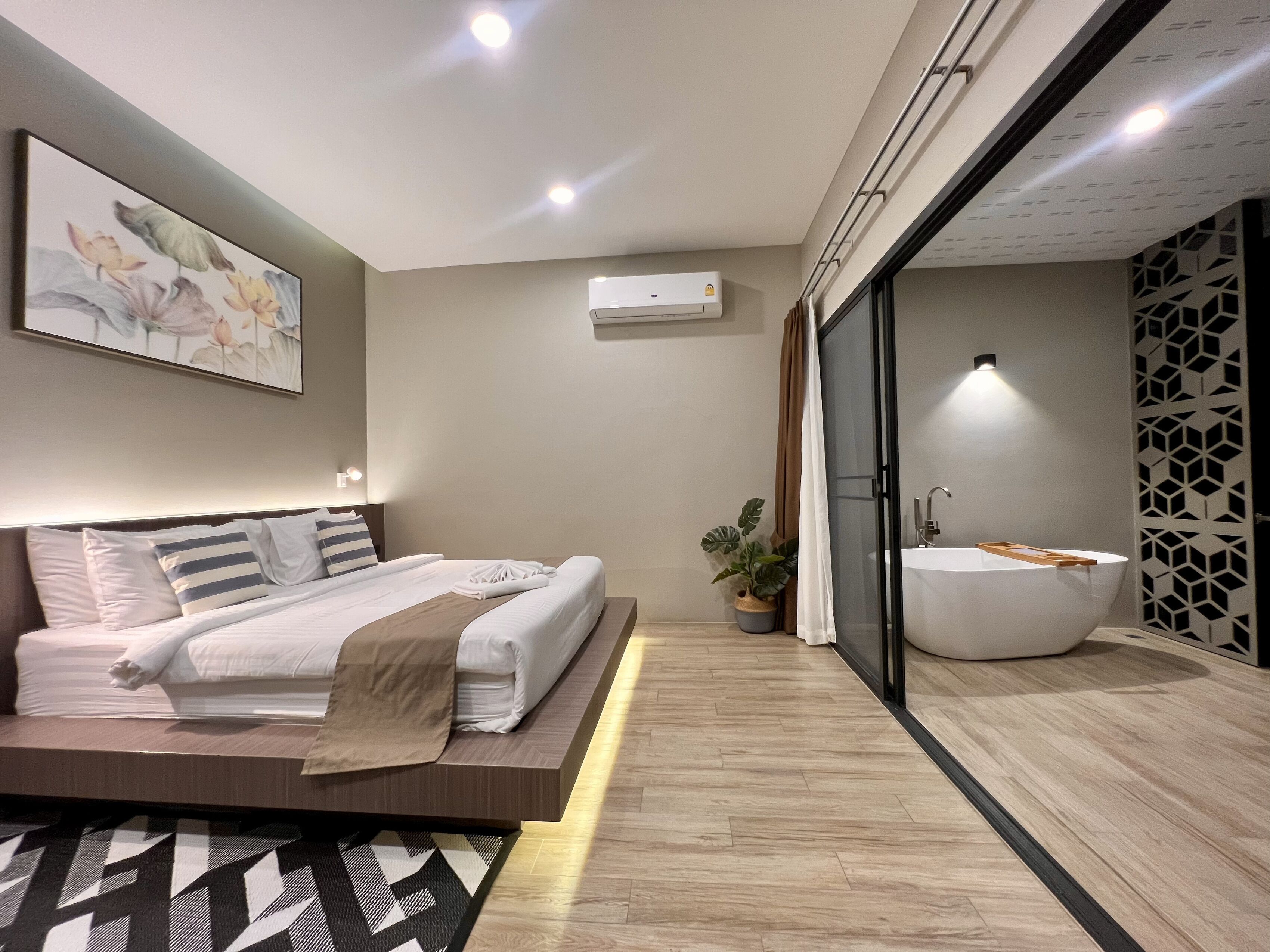 A modern bedroom with a large bed, a bedside table, a wall-mounted air conditioner, and a bathroom with a bathtub.