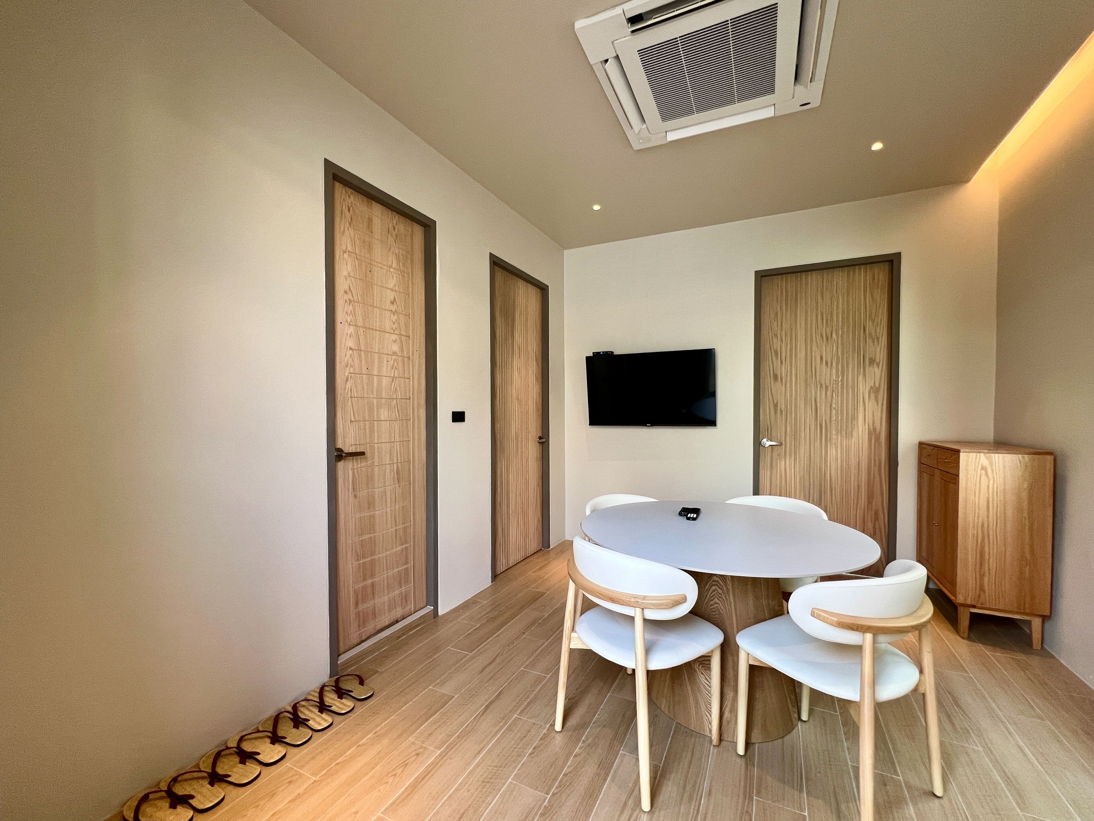 Quarto moderno com mesa redonda, quatro cadeiras, televisão de tela plana e armário de madeira.