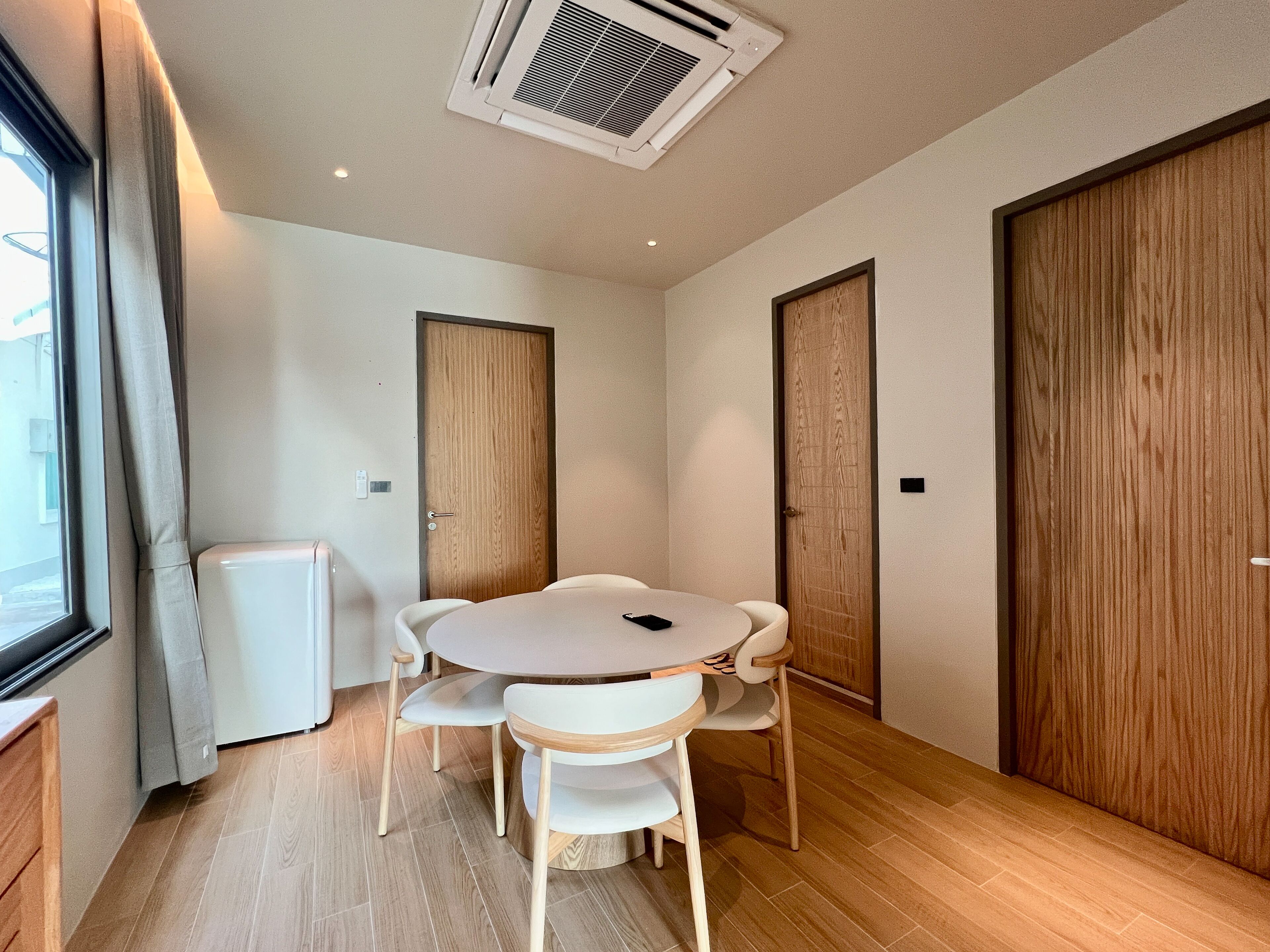 A modern room with a round table and chairs, wooden doors, and a window with curtains.