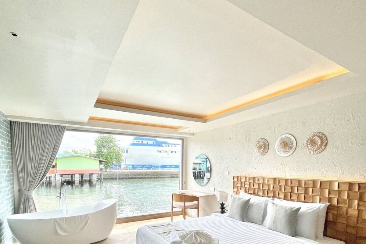 Een moderne slaapkamer met een groot bed, een badkuip en uitzicht op een waterpartij.