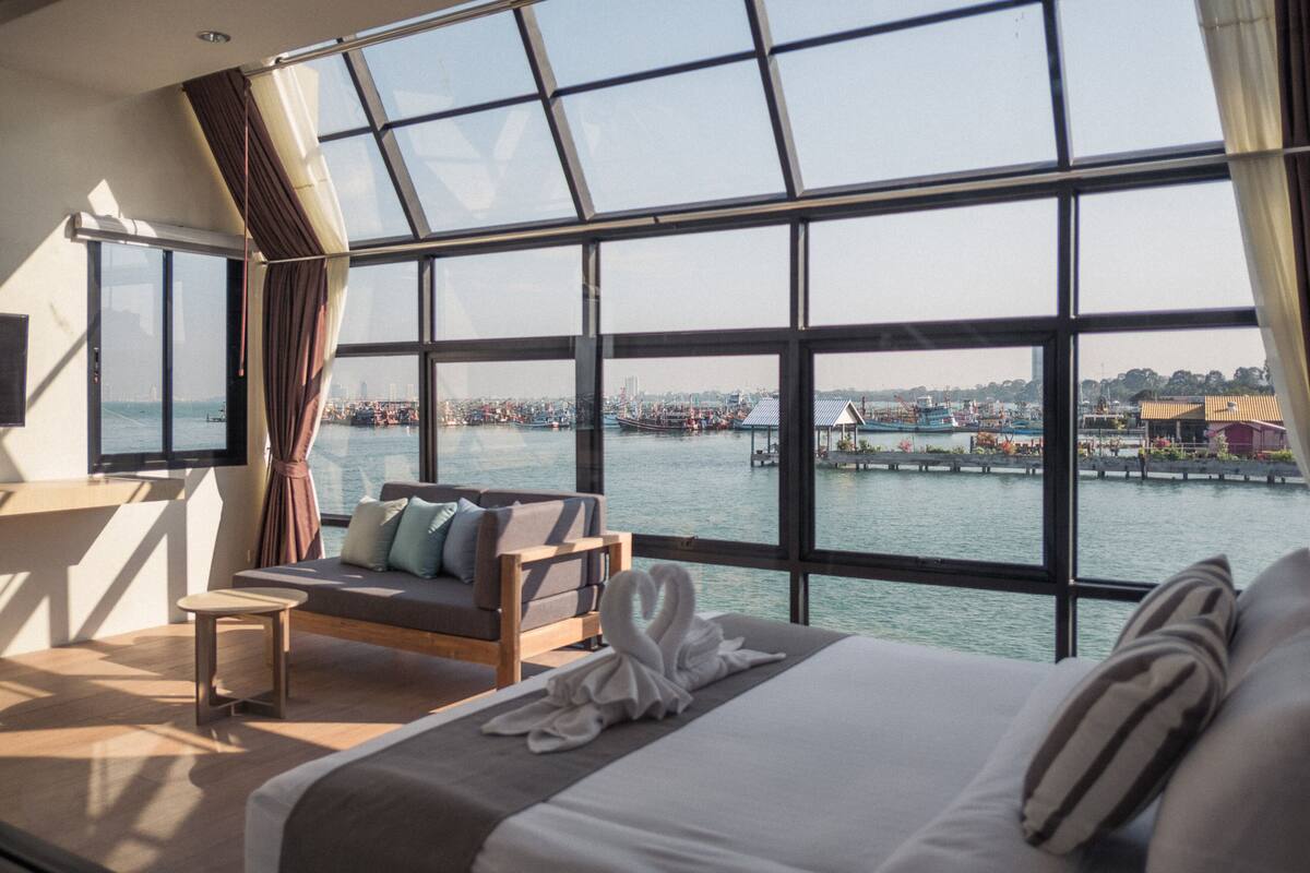 Een hotelkamer met een groot raam met uitzicht op een waterkant, een bed, een bank en een klein tafeltje.