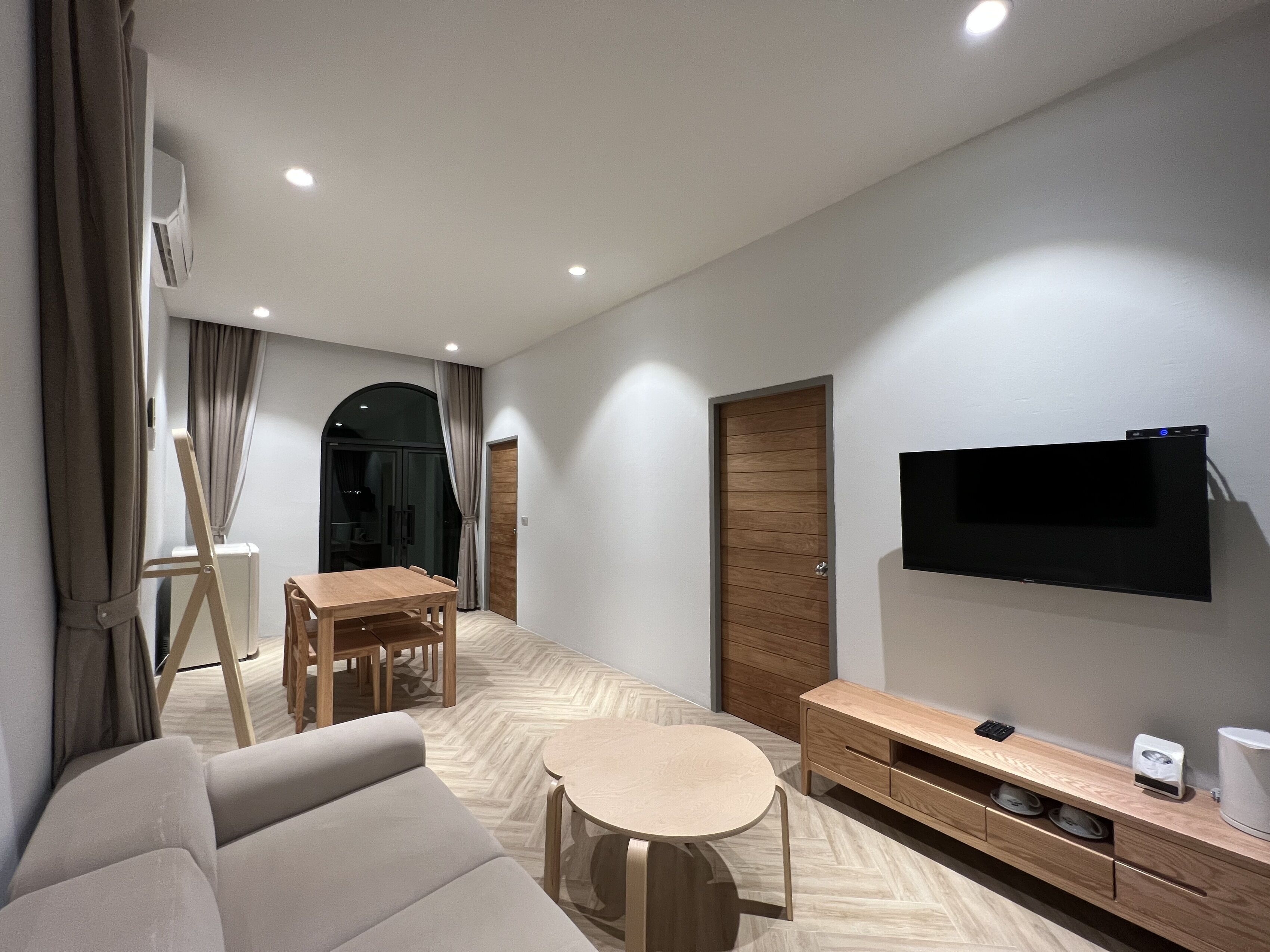 A modern living room with a sofa, a dining table, and a TV mounted on the wall.