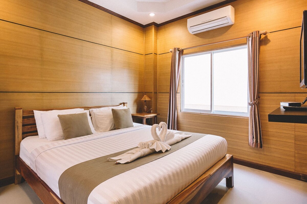 Une chambre d’hôtel avec un grand lit, des murs en bois, un appareil de climatisation, une fenêtre avec des rideaux et une table de chevet avec une lampe.