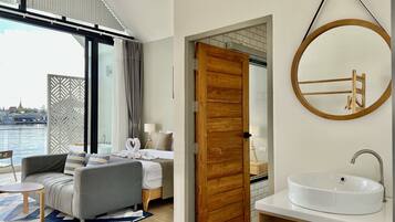 A modern hotel room with a large window, a round mirror, a wooden door, and a white sink.