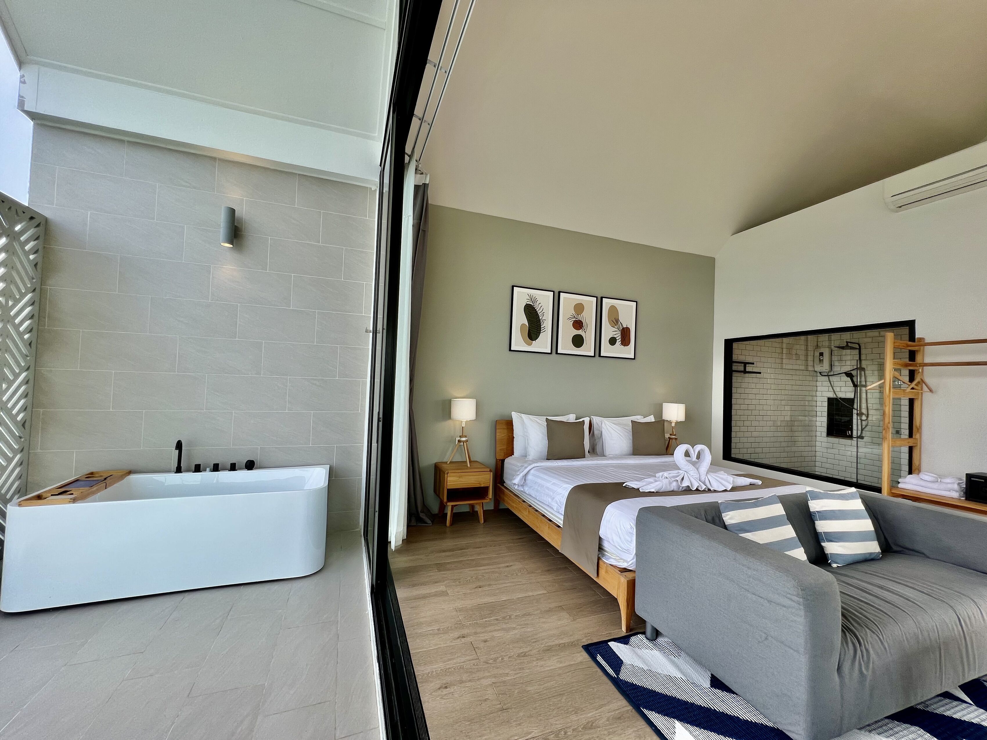 A modern hotel room with a large bed, a sofa, a bathtub, and a shower area.