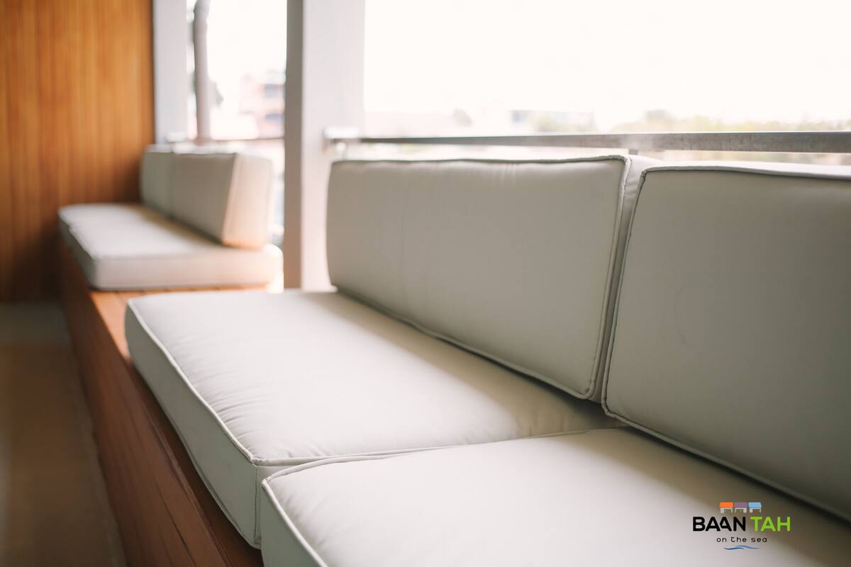 Een rij witte, beklede banken met een houten vloer en uitzicht op zee.