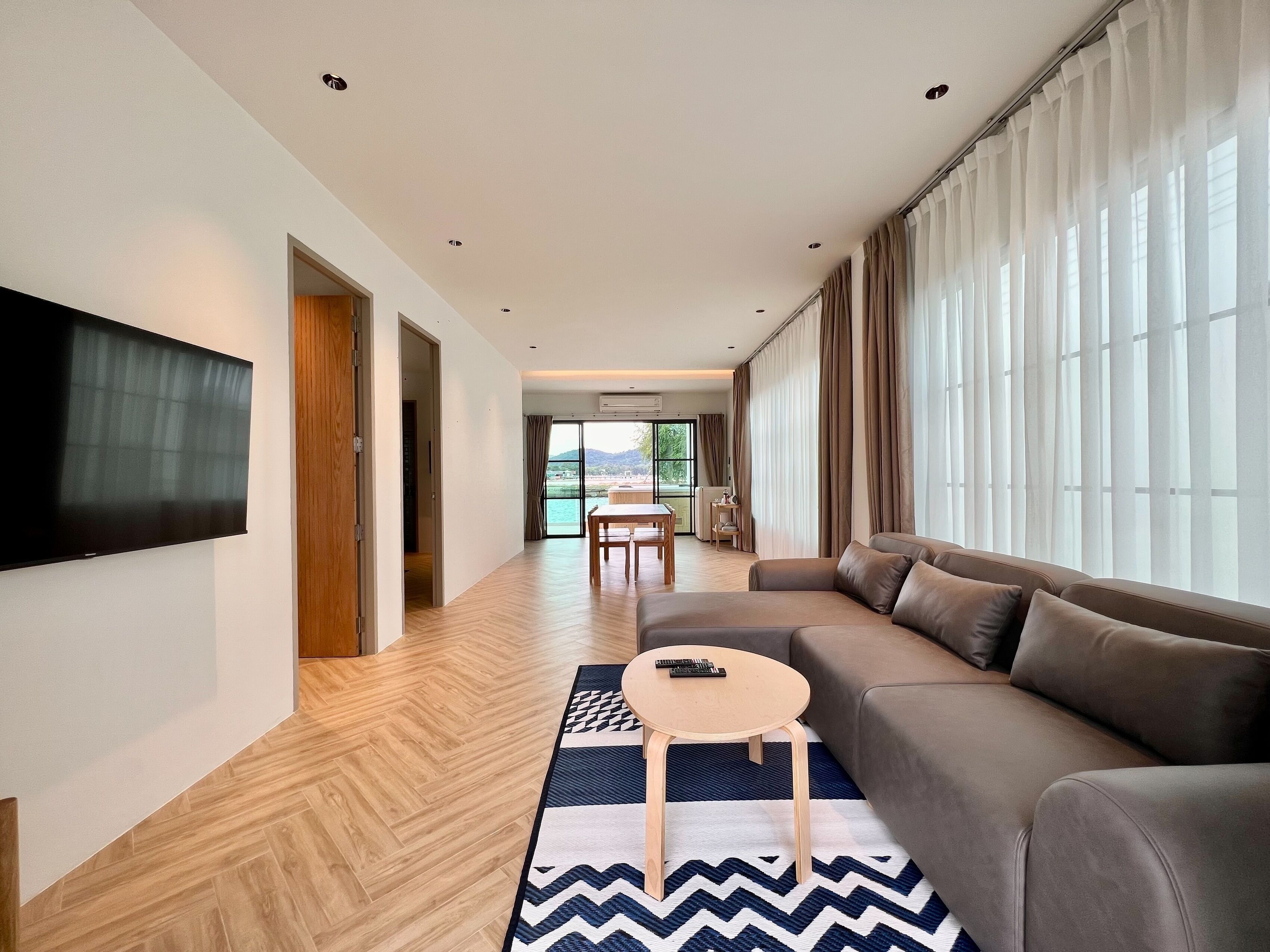 A modern living room with a large flat-screen TV, a sofa, a coffee table, and a patterned rug.