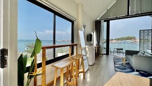 Una habitación moderna con amplios ventanales que dan a un puerto deportivo, un escritorio de madera, un sofá y vistas a barcos y edificios al otro lado del agua.