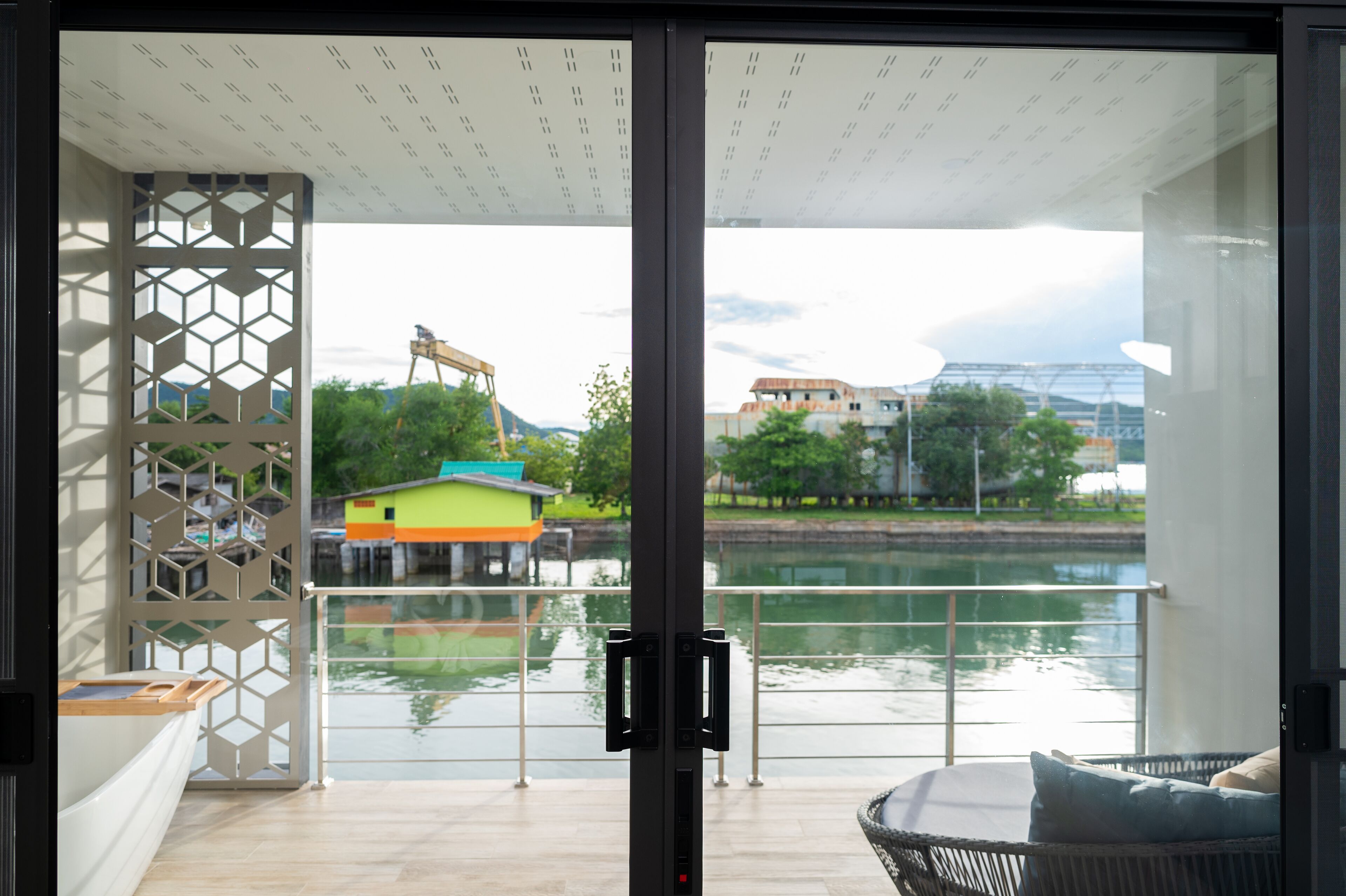 A modern room with a glass door leading to a balcony overlooking a river and buildings.