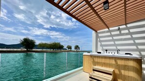 Una terraza de madera con vista al mar y árboles, un banco de madera y un lavamanos moderno.