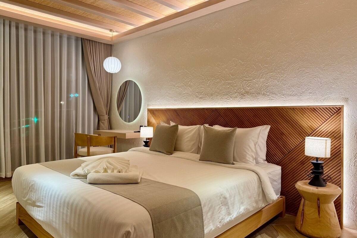 Een moderne hotelkamer met een groot bed, een houten hoofdbord, een ronde spiegel en twee nachtkastjes met lampen.