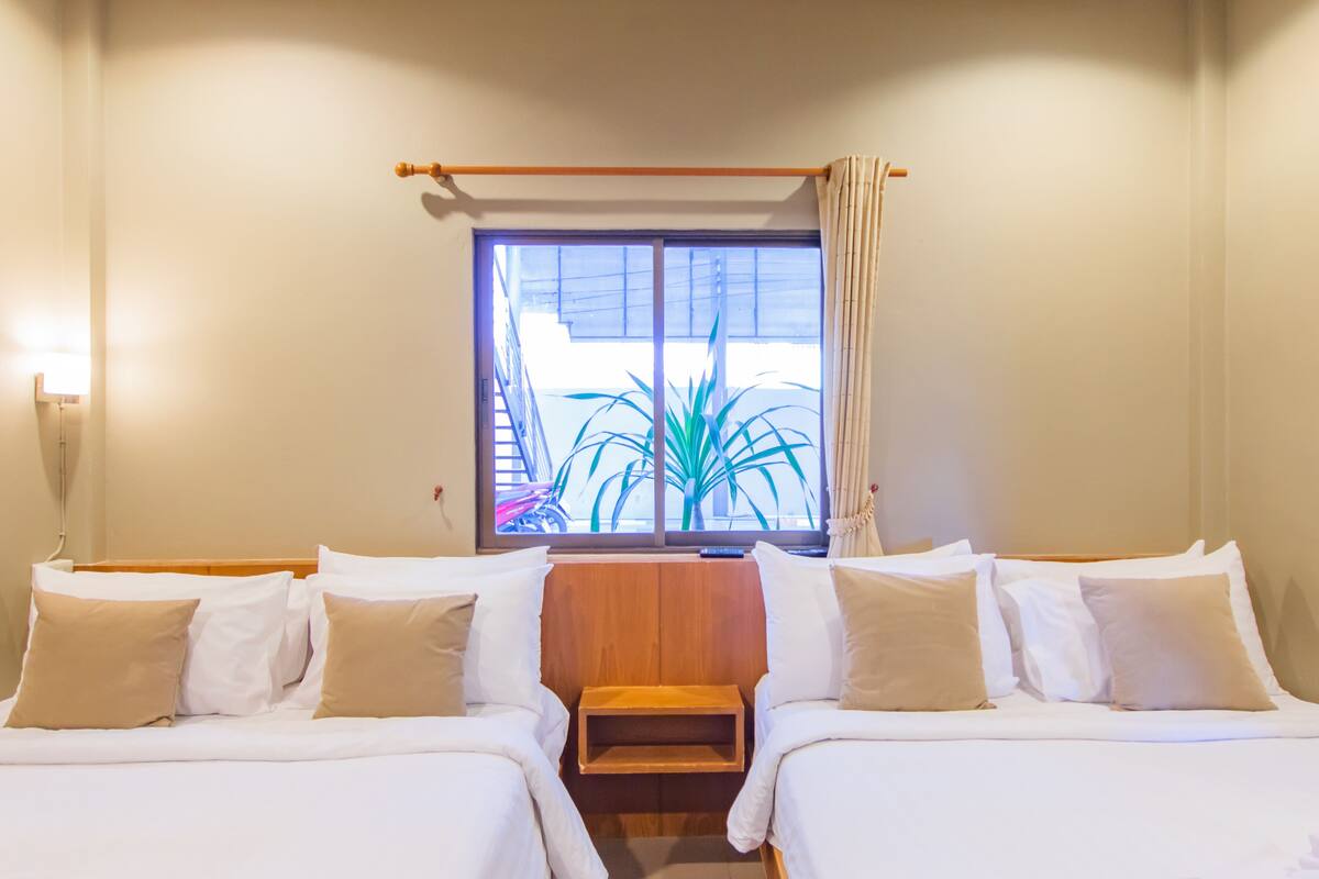 Een hotelkamer met twee bedden, een raam met gordijnen, een houten hoofdeinde en een nachtkastje.