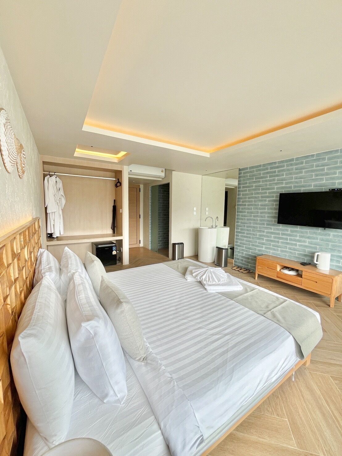 A hotel room with a large bed, a TV, a wooden dresser, and a bathroom visible through an open door.