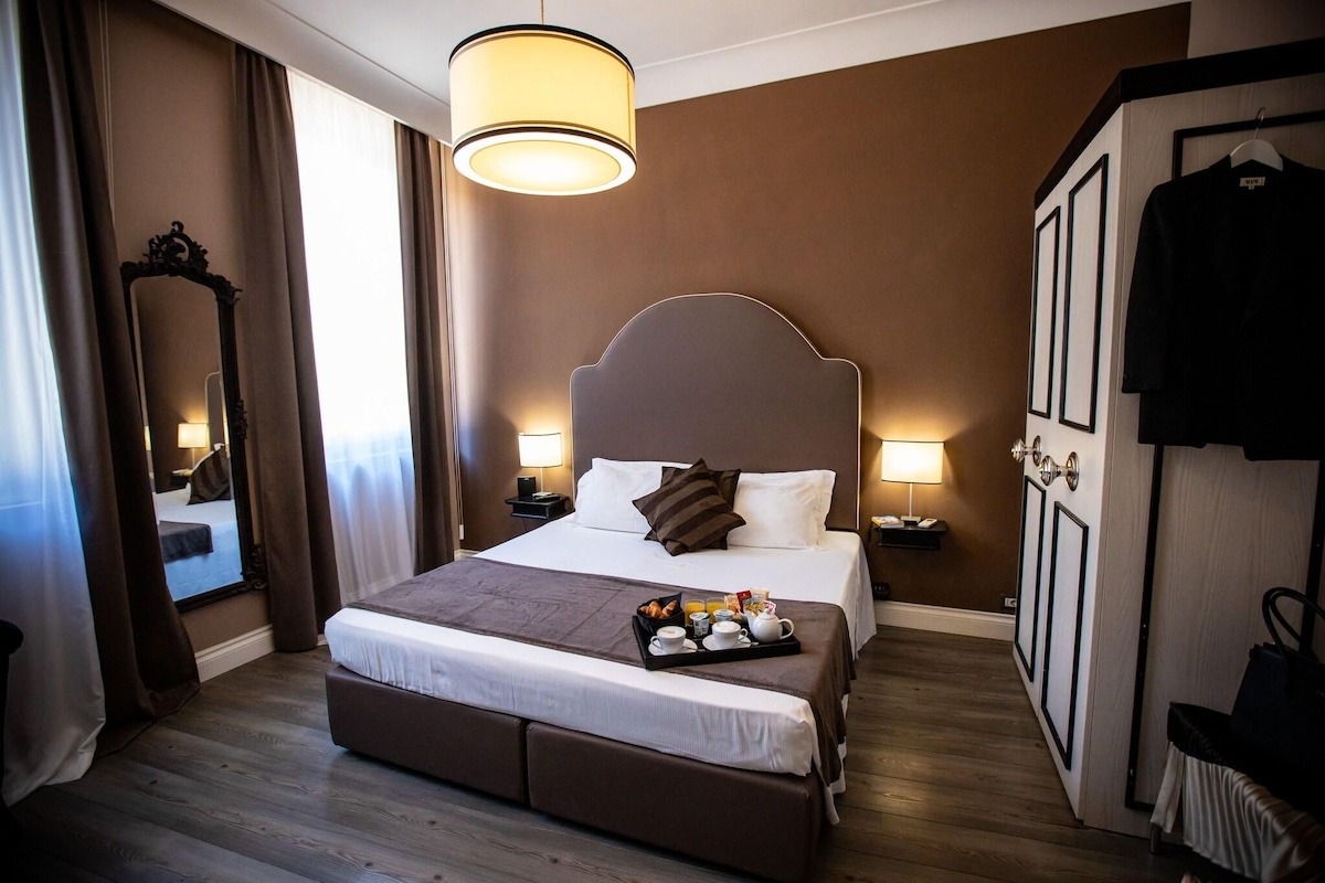 Una habitación de hotel con una cama grande, lámparas de noche, un armario y una bandeja de desayuno sobre la cama.