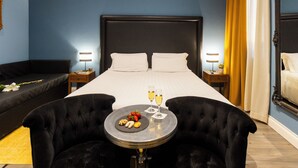 Una habitación de hotel con una cama grande, un sofá, una mesa redonda con comida y bebidas, y dos lámparas de noche.