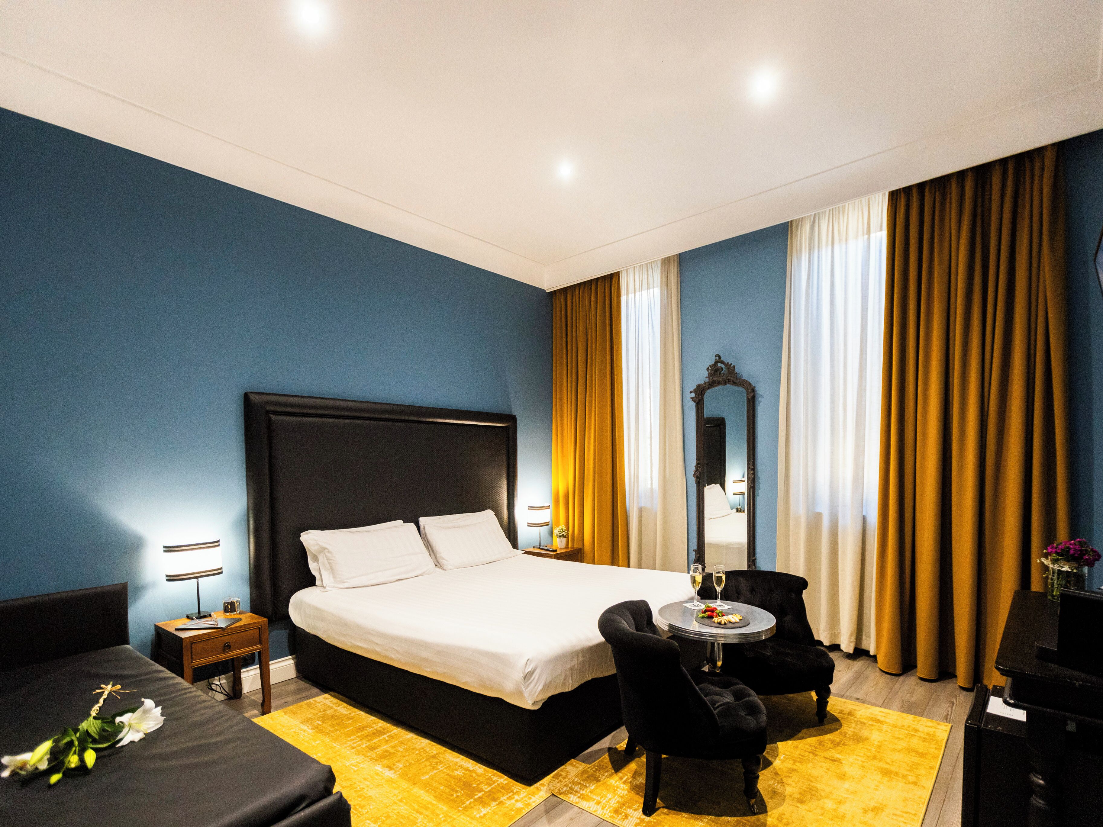 A hotel room with a large bed, a small round table with two chairs, a nightstand, and a mirror.