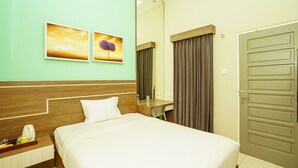 A hotel room with a bed, bedside table, mirror, and a door. - Ardhya Guesthouse Syariah by Ecommerceloka (Sidoarjo)